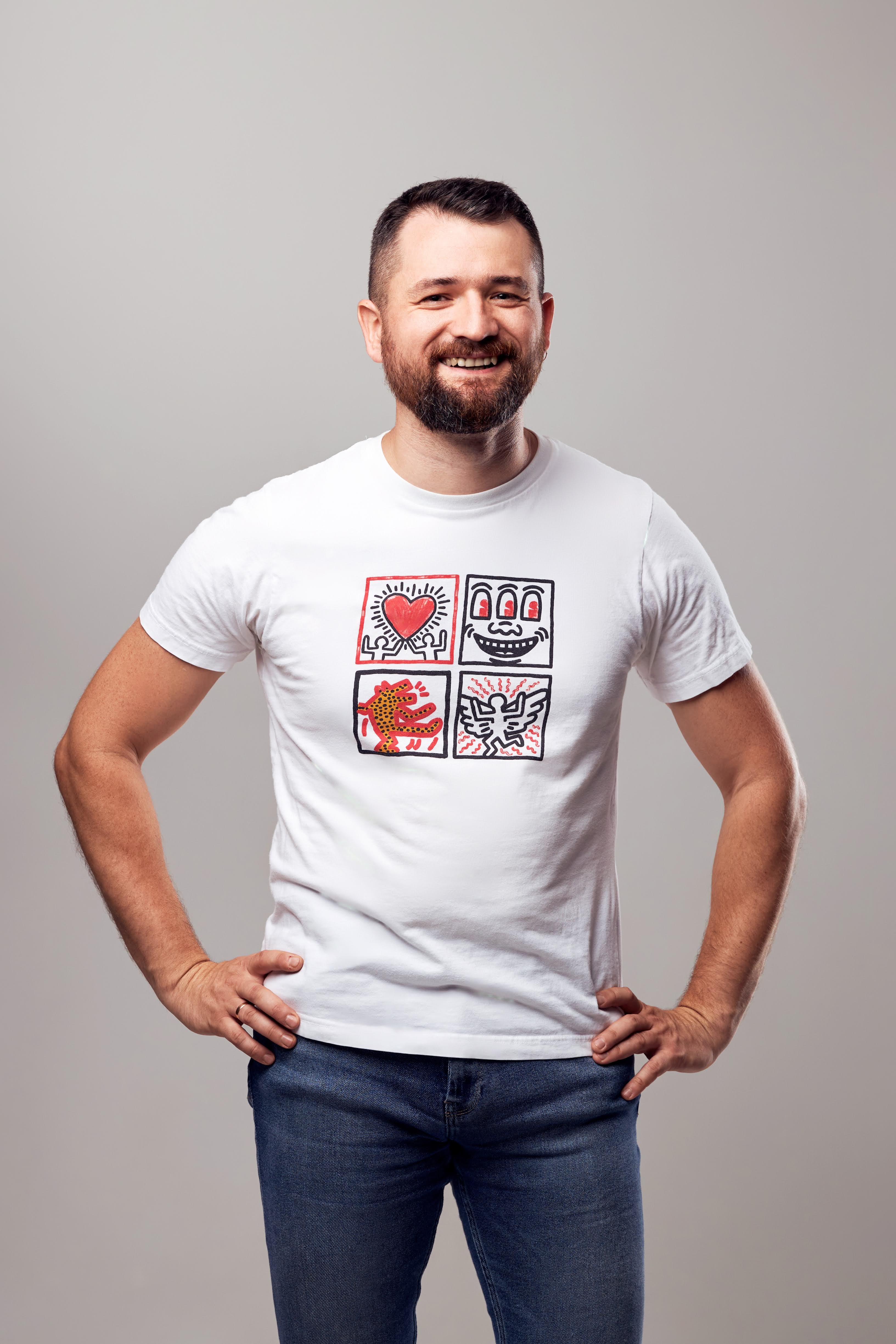 A model wearing a white t-shirt with Keith Haring style artwork featuring four squares containing heart, face, figure and bird designs in red and black