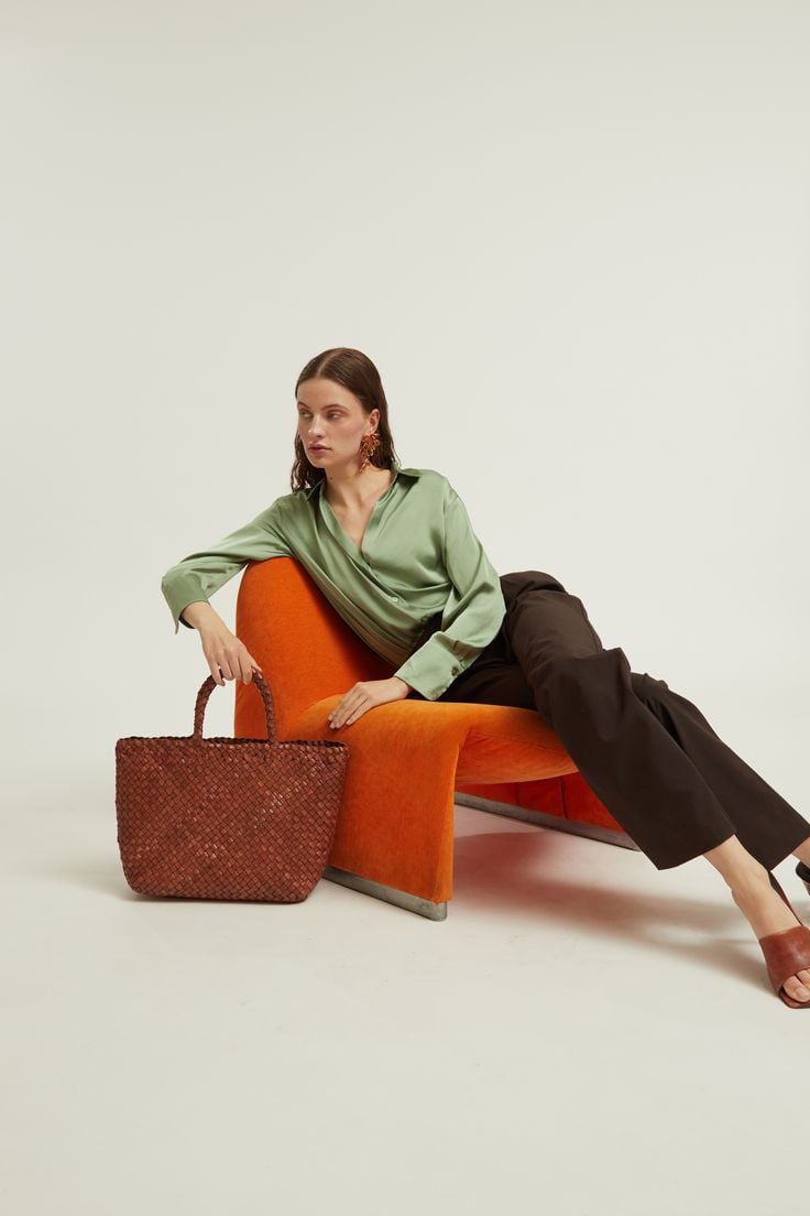 Model in sage silk and chocolate trousers on tangerine velvet chair