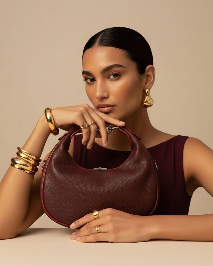Model with gold jewelry and burgundy bag in warm beige studio
