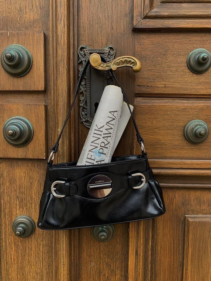 Glossy black patent leather bag hanging from an ornate brass door handle on a carved wooden door