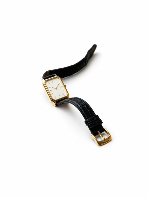 Vintage gold rectangular dress watch with a cream dial, gold indices, and a black croc-embossed leather strap, displayed flat on a white background.