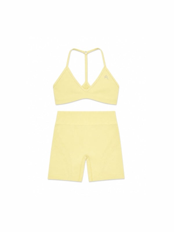 Pale yellow bralette with criss-cross back straps and matching high-waisted bike shorts, displayed flat on a white background.