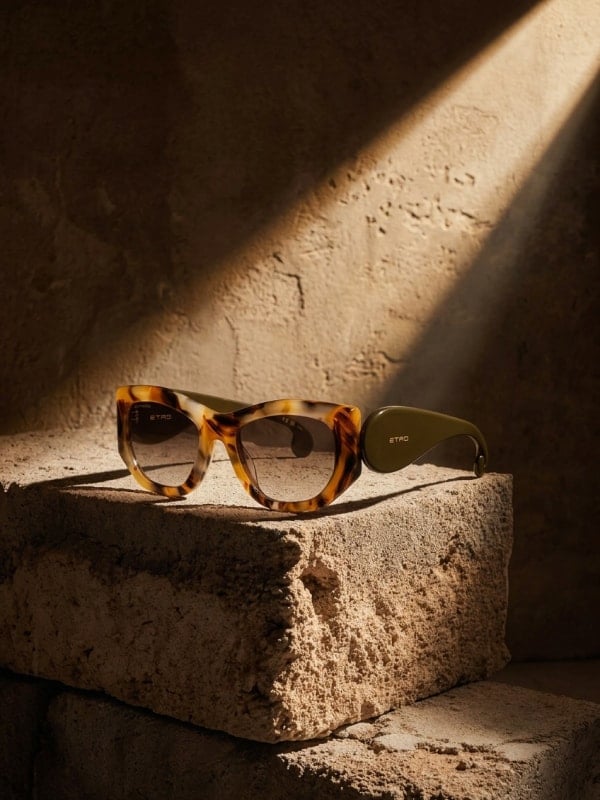 Tortoiseshell Etro butterfly sunglasses placed on a textured travertine block in dramatic directional sunlight, against a warm tan wall.