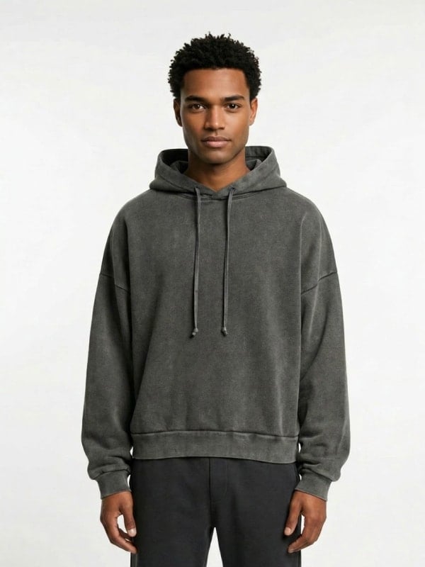 Man in a charcoal washed hoodie and black sweatpants photographed against a clean white studio background.