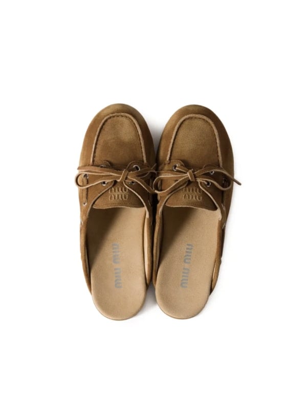 Pair of tan suede Miu Miu boat shoes shown top-down on a white background, with brown laces and embroidered logo on the tongue.