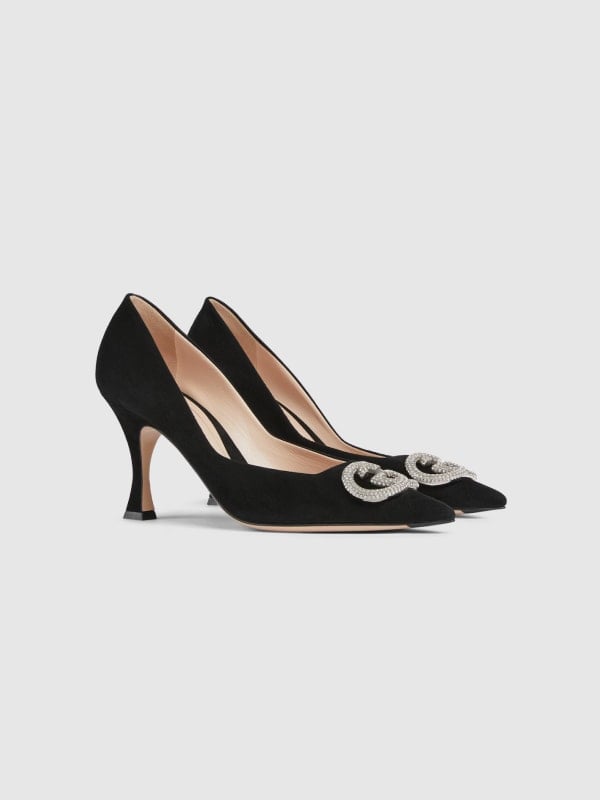 Pair of black suede Gucci pointed-toe heels with crystal GG buckles, shown in three-quarter view on a light background.