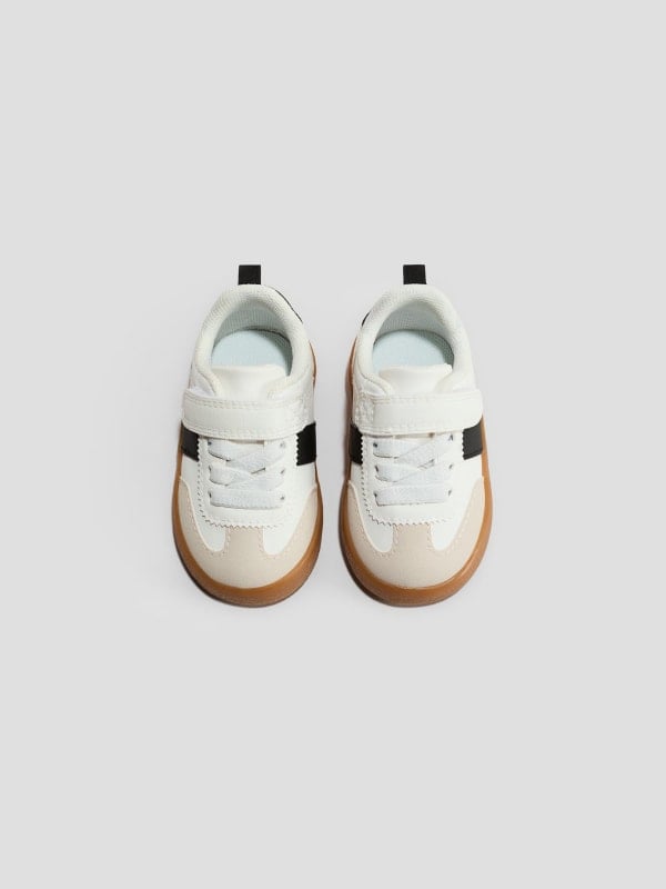 Kids' white sneakers with velcro strap, beige panels, and gum soles, shown top-down on a light grey background.