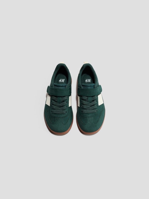 Pair of dark green H&M kids' suede sneakers with velcro strap and gum soles, shown top-down on a light background.