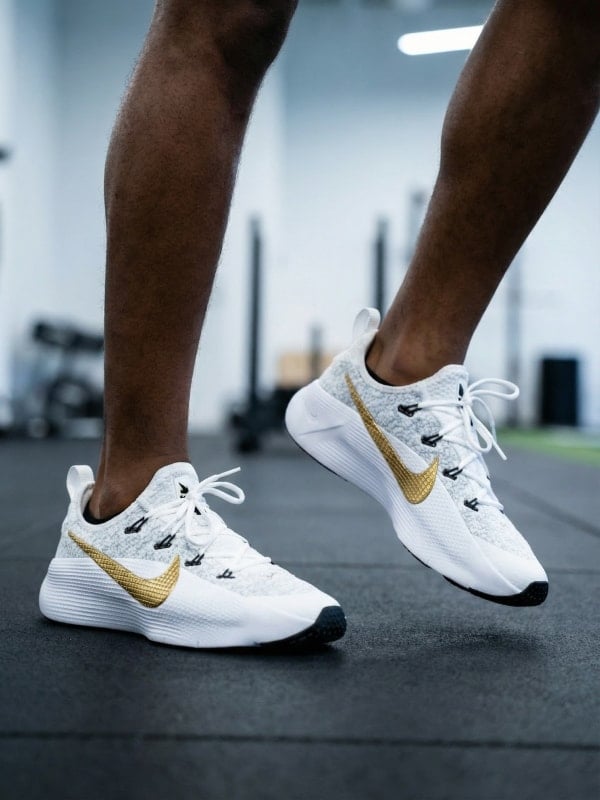 Cropped shot of a man mid-stride in a gym wearing white Nike running shoes with gold swooshes.