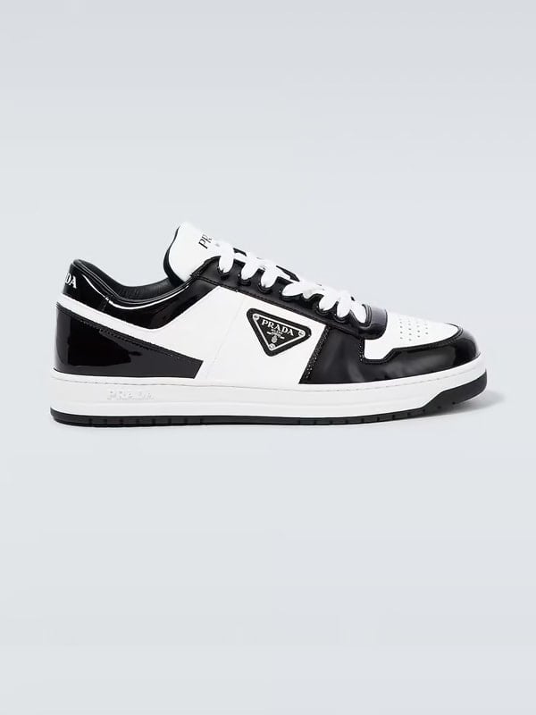 Side view of a Prada low-top sneaker in black and white patent leather with the signature triangle logo on the side, displayed on a light background.