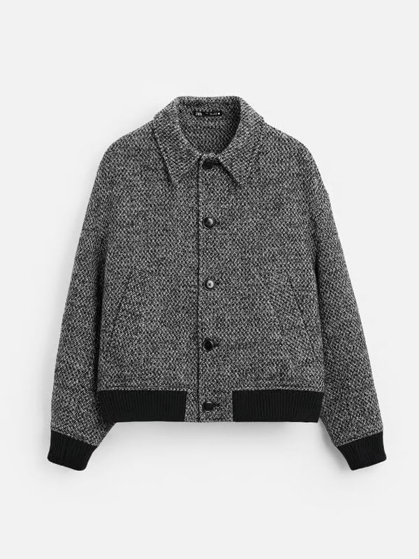 Flat lay of a textured grey button-up jacket with black ribbed cuffs and hem, displayed on a white background.