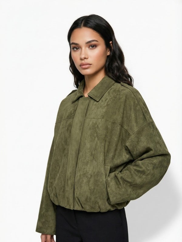 Woman with long dark hair wearing an olive green suede bomber jacket, photographed in a clean studio setting.