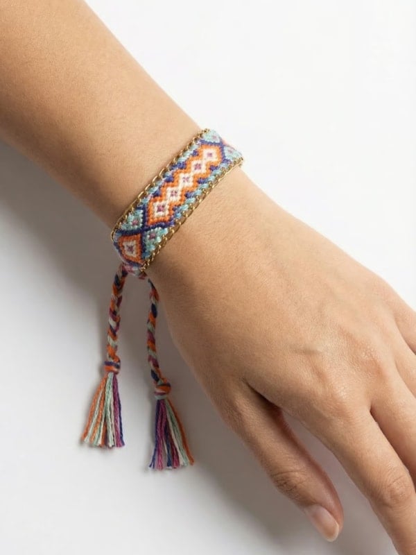 Close-up of a wrist wearing a colourful woven friendship bracelet with tassel ties, against a clean light background.