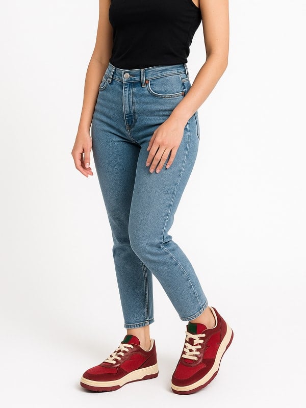 Woman wearing high-waisted blue jeans, a black tank top, and red sneakers with cream laces, posing against a white background.