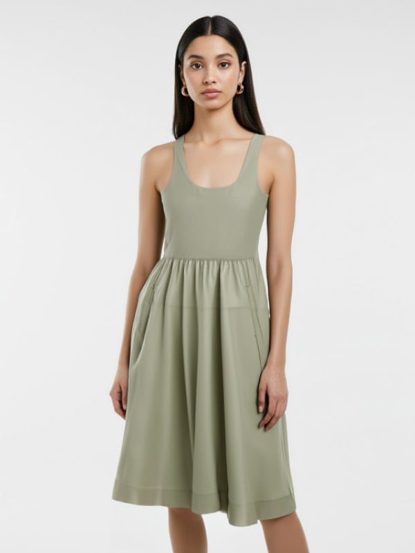 Woman in a sleeveless, sage green midi dress with a gathered waist, standing against a light background.
