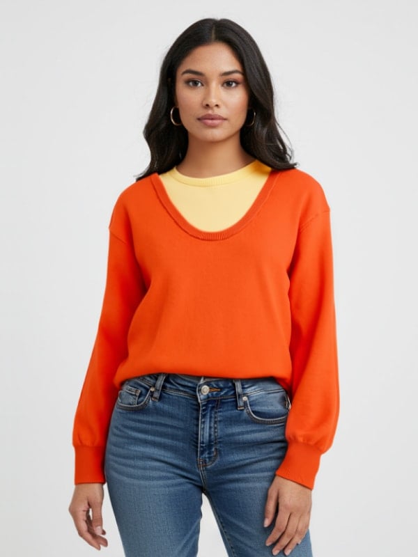 Woman wearing an orange V-neck sweater layered over a yellow top, paired with blue jeans, standing against a light background.