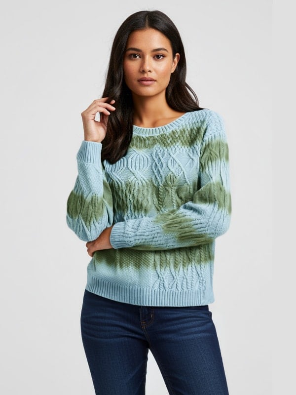 Woman in a light blue and green tie-dye knit sweater with dark denim jeans, posing against a plain background.