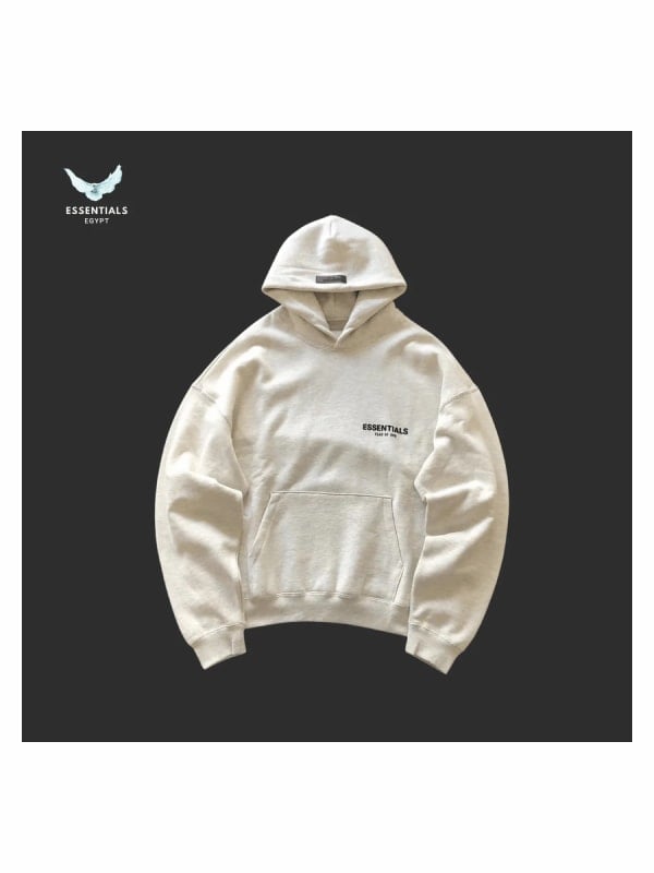 Cream Essentials oversized hoodie with black centre-chest text logo, displayed against a dark grey background.